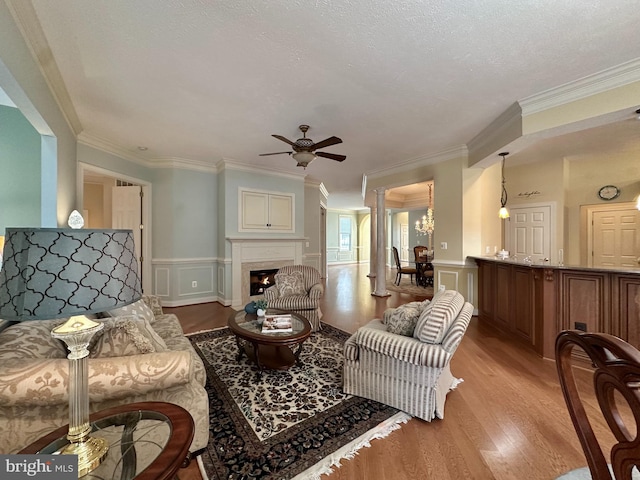 living room with a fireplace, light wood-type flooring, ornamental molding, ceiling fan, and a textured ceiling