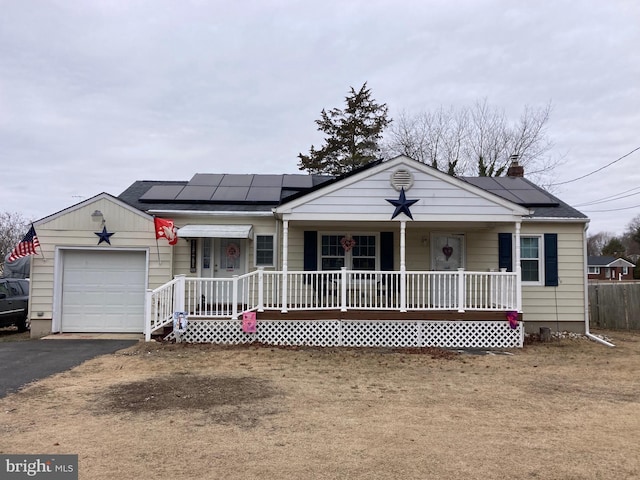 single story home with aphalt driveway, covered porch, roof mounted solar panels, and an attached garage