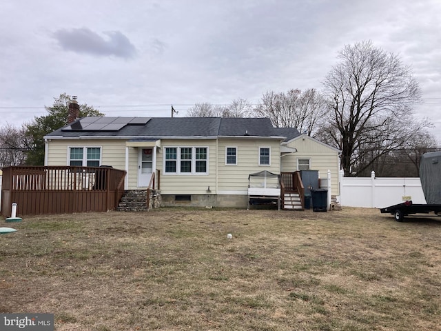 rear view of house with a shingled roof, a yard, fence, a wooden deck, and roof mounted solar panels