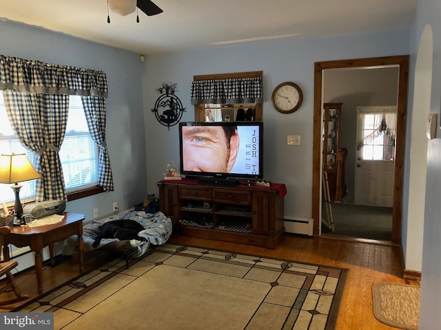 living room with a baseboard heating unit, a wealth of natural light, wood-type flooring, and ceiling fan