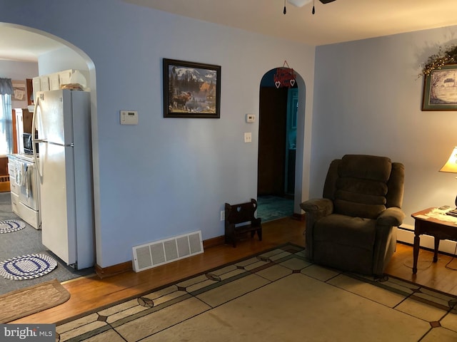 living room with arched walkways, visible vents, baseboard heating, ceiling fan, and wood finished floors