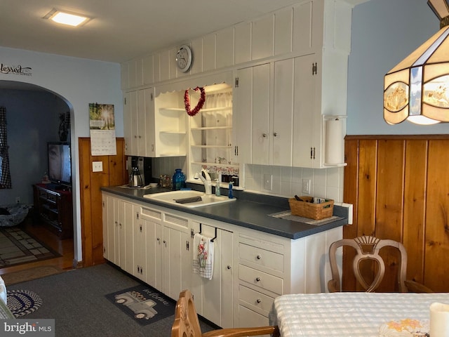 kitchen featuring dark countertops, a wainscoted wall, white cabinets, and a sink