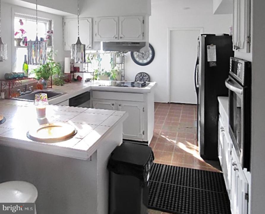 kitchen featuring stainless steel appliances, white cabinets, decorative light fixtures, tile countertops, and kitchen peninsula