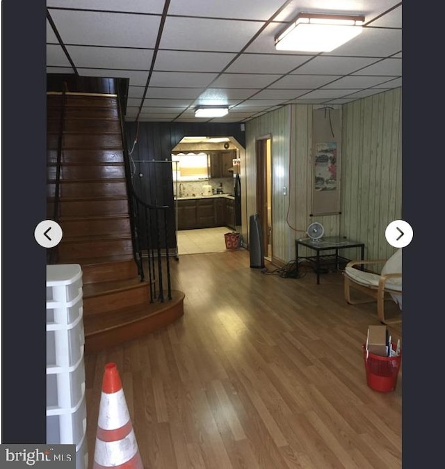 basement featuring a paneled ceiling, hardwood / wood-style floors, and wooden walls