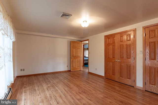 unfurnished bedroom featuring baseboard heating and light hardwood / wood-style flooring