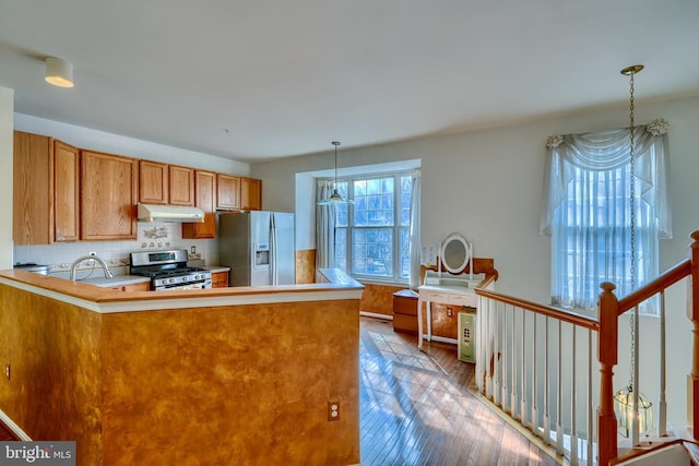 kitchen with appliances with stainless steel finishes, decorative light fixtures, light hardwood / wood-style floors, and kitchen peninsula