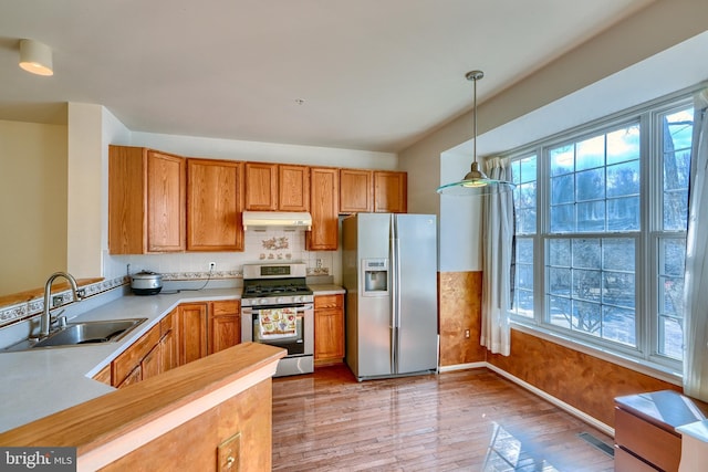 kitchen with appliances with stainless steel finishes, sink, decorative backsplash, hanging light fixtures, and light wood-type flooring