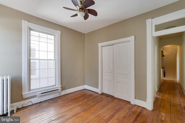 unfurnished bedroom featuring arched walkways, baseboards, hardwood / wood-style floors, and radiator