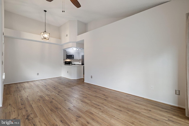 unfurnished living room featuring high vaulted ceiling, ceiling fan with notable chandelier, and light hardwood / wood-style floors