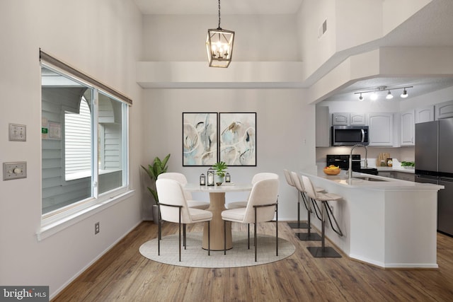 dining area with sink, wood-type flooring, a chandelier, and a high ceiling