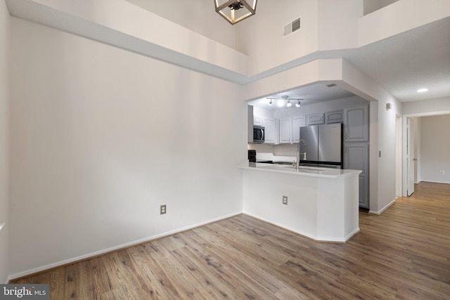 kitchen featuring kitchen peninsula, hardwood / wood-style flooring, stainless steel appliances, a high ceiling, and white cabinets