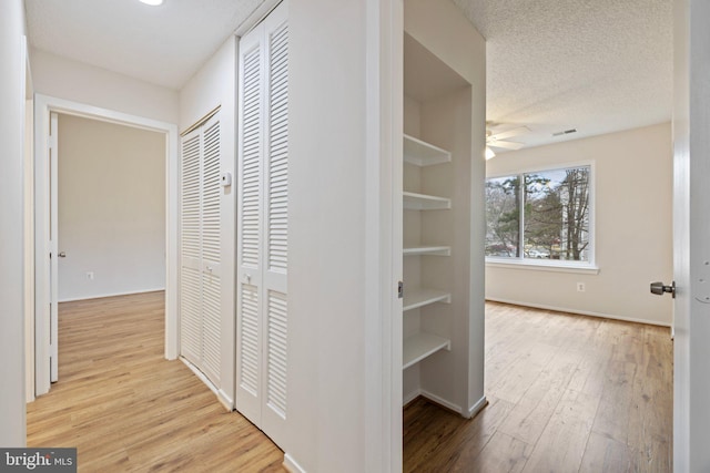 corridor featuring a textured ceiling, light hardwood / wood-style floors, and built in shelves