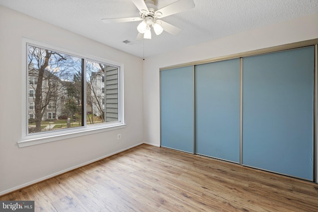 unfurnished bedroom with ceiling fan, a closet, wood-type flooring, and a textured ceiling