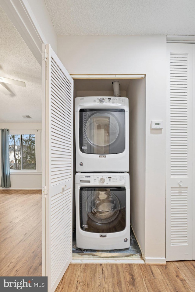 clothes washing area featuring wood-type flooring, stacked washing maching and dryer, and a textured ceiling