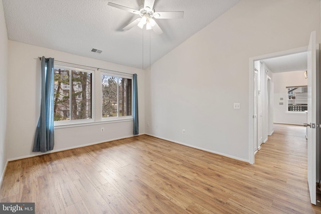 spare room with ceiling fan, lofted ceiling, a textured ceiling, and light hardwood / wood-style floors