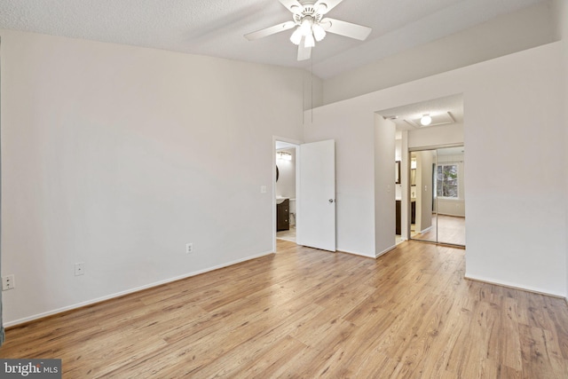 spare room with ceiling fan, lofted ceiling, a textured ceiling, and light wood-type flooring