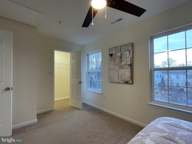 bedroom featuring light colored carpet, a walk in closet, and multiple windows