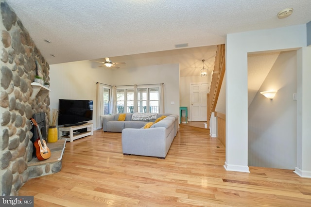 living room with visible vents, a ceiling fan, a textured ceiling, light wood-type flooring, and stairs