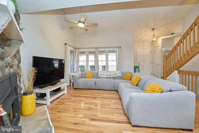 living room featuring light wood-style floors, ceiling fan with notable chandelier, high vaulted ceiling, and stairs