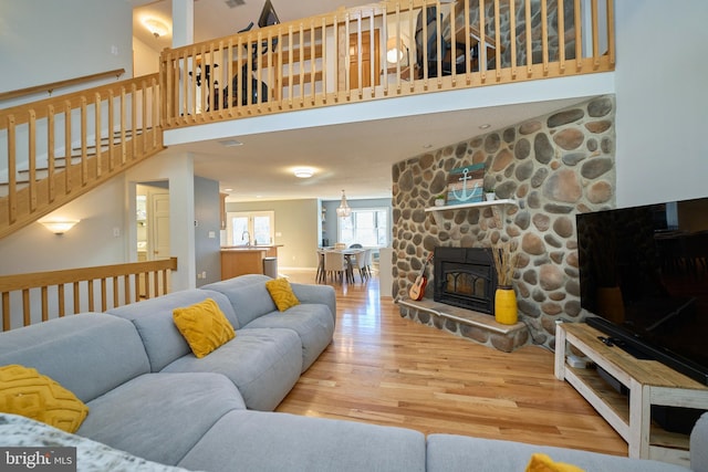 living room featuring a towering ceiling, stairway, wood finished floors, and a stone fireplace