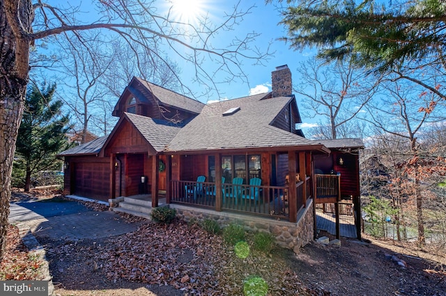 view of front of house featuring roof with shingles, a chimney, a porch, an attached garage, and driveway