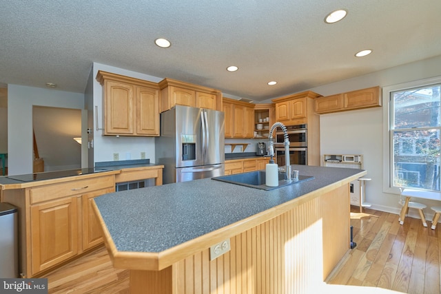 kitchen with stainless steel appliances, dark countertops, light wood-style floors, a sink, and an island with sink