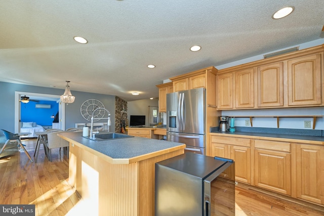 kitchen featuring stainless steel fridge with ice dispenser, an island with sink, light wood-style flooring, pendant lighting, and a sink