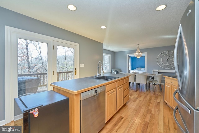 kitchen featuring light wood finished floors, appliances with stainless steel finishes, a kitchen island with sink, pendant lighting, and a sink