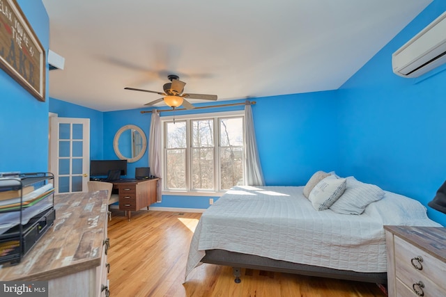 bedroom featuring light wood-type flooring, baseboards, a ceiling fan, and a wall mounted air conditioner