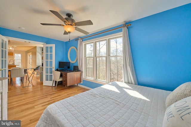 bedroom featuring a sink, a ceiling fan, baseboards, french doors, and light wood finished floors