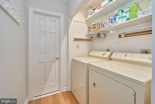 clothes washing area with laundry area, washing machine and dryer, and light wood-style flooring