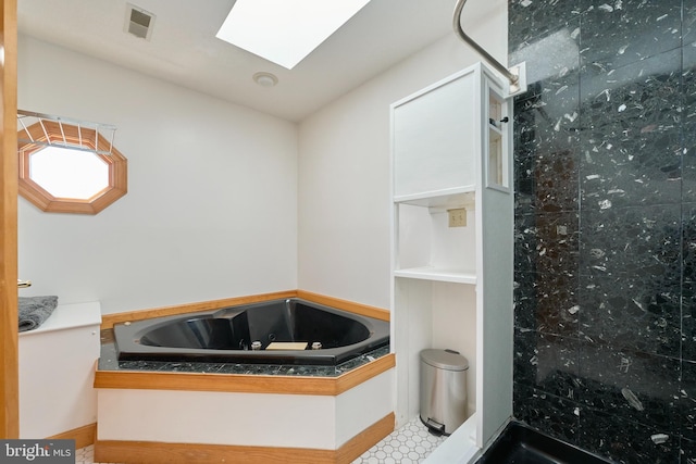 bathroom with a jetted tub, a skylight, visible vents, and tiled shower