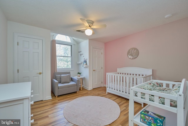 bedroom with visible vents, light wood-style floors, ceiling fan, a textured ceiling, and a nursery area