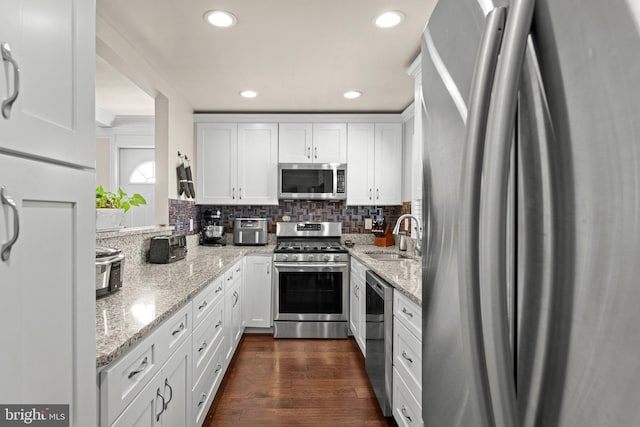 kitchen with stainless steel appliances, dark wood-type flooring, a sink, white cabinets, and tasteful backsplash