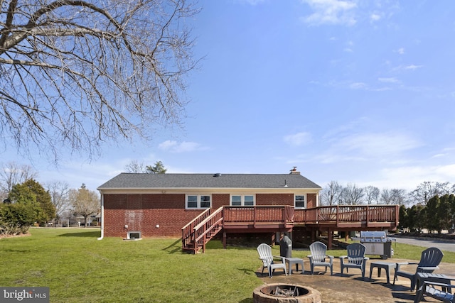 rear view of property featuring an outdoor fire pit, brick siding, a lawn, and a deck