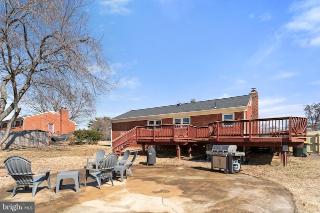 back of property featuring a deck, a patio, brick siding, stairs, and a chimney