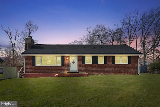 ranch-style house featuring brick siding, a shingled roof, fence, a lawn, and a chimney