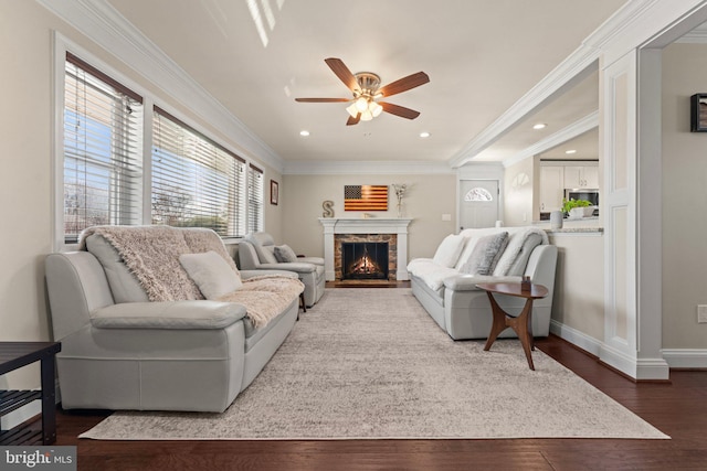 living room featuring crown molding, recessed lighting, a ceiling fan, wood finished floors, and a warm lit fireplace