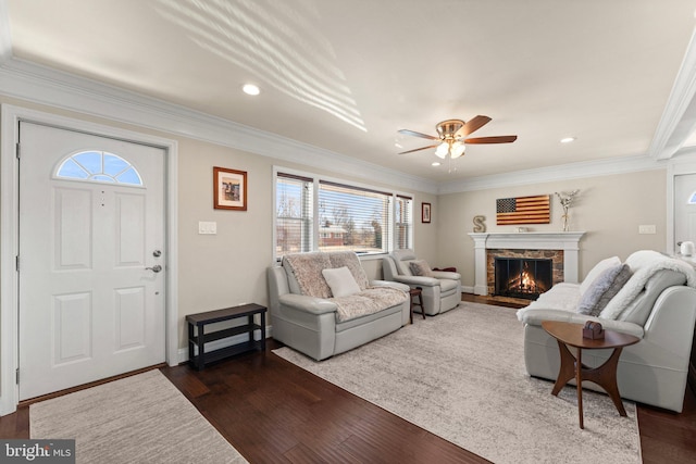 living room featuring recessed lighting, ornamental molding, dark wood-type flooring, and a stone fireplace