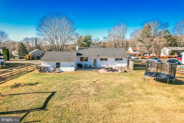 back of property with a trampoline, a yard, and a patio area