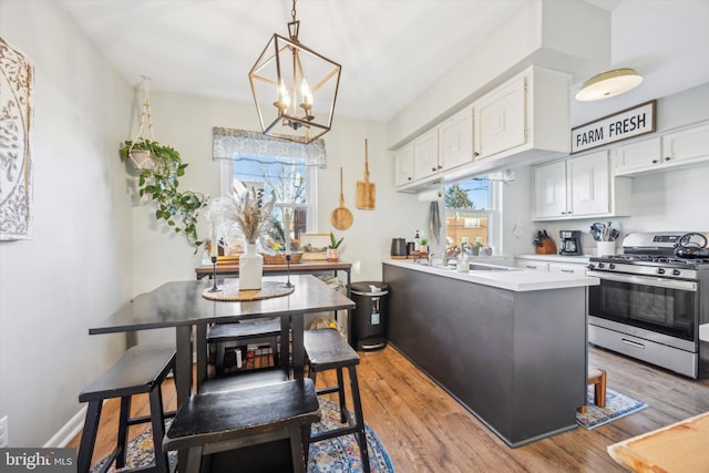 kitchen with stainless steel gas stove, white cabinetry, hanging light fixtures, kitchen peninsula, and light hardwood / wood-style floors