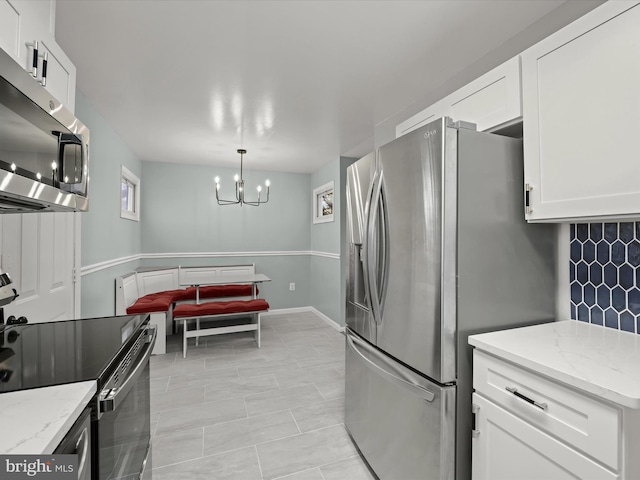 kitchen featuring white cabinets, pendant lighting, stainless steel appliances, light stone countertops, and backsplash