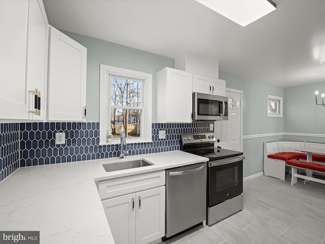 kitchen featuring sink, white cabinets, backsplash, stainless steel appliances, and light stone countertops