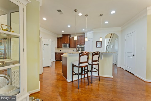 kitchen featuring visible vents, arched walkways, hanging light fixtures, light stone countertops, and stainless steel appliances