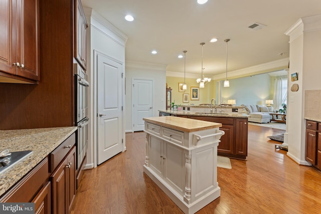 kitchen featuring visible vents, wood counters, a center island, light wood-type flooring, and a sink