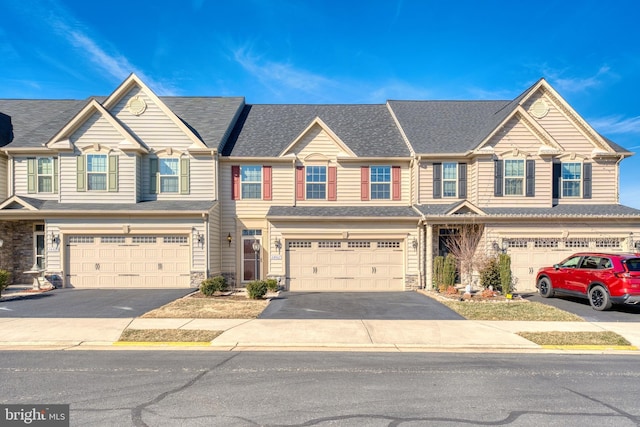 view of property featuring a shingled roof, stone siding, driveway, and an attached garage