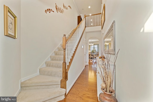 stairway with a chandelier, a towering ceiling, baseboards, and wood finished floors