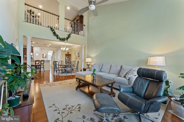 living area with ceiling fan with notable chandelier, decorative columns, a high ceiling, and wood finished floors