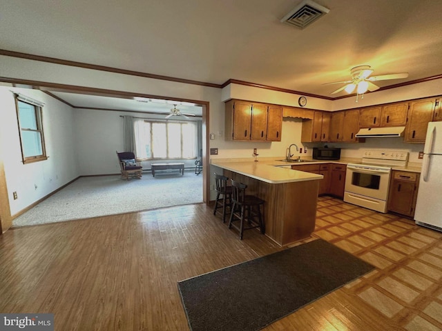 kitchen featuring light countertops, a sink, a peninsula, white appliances, and under cabinet range hood