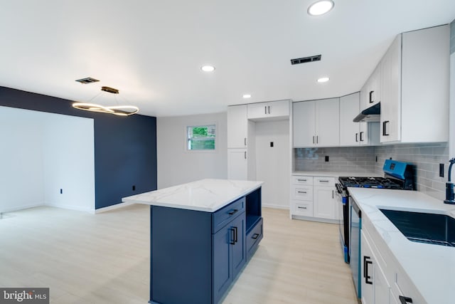 kitchen featuring stainless steel gas range, white cabinetry, tasteful backsplash, a kitchen island, and light stone countertops